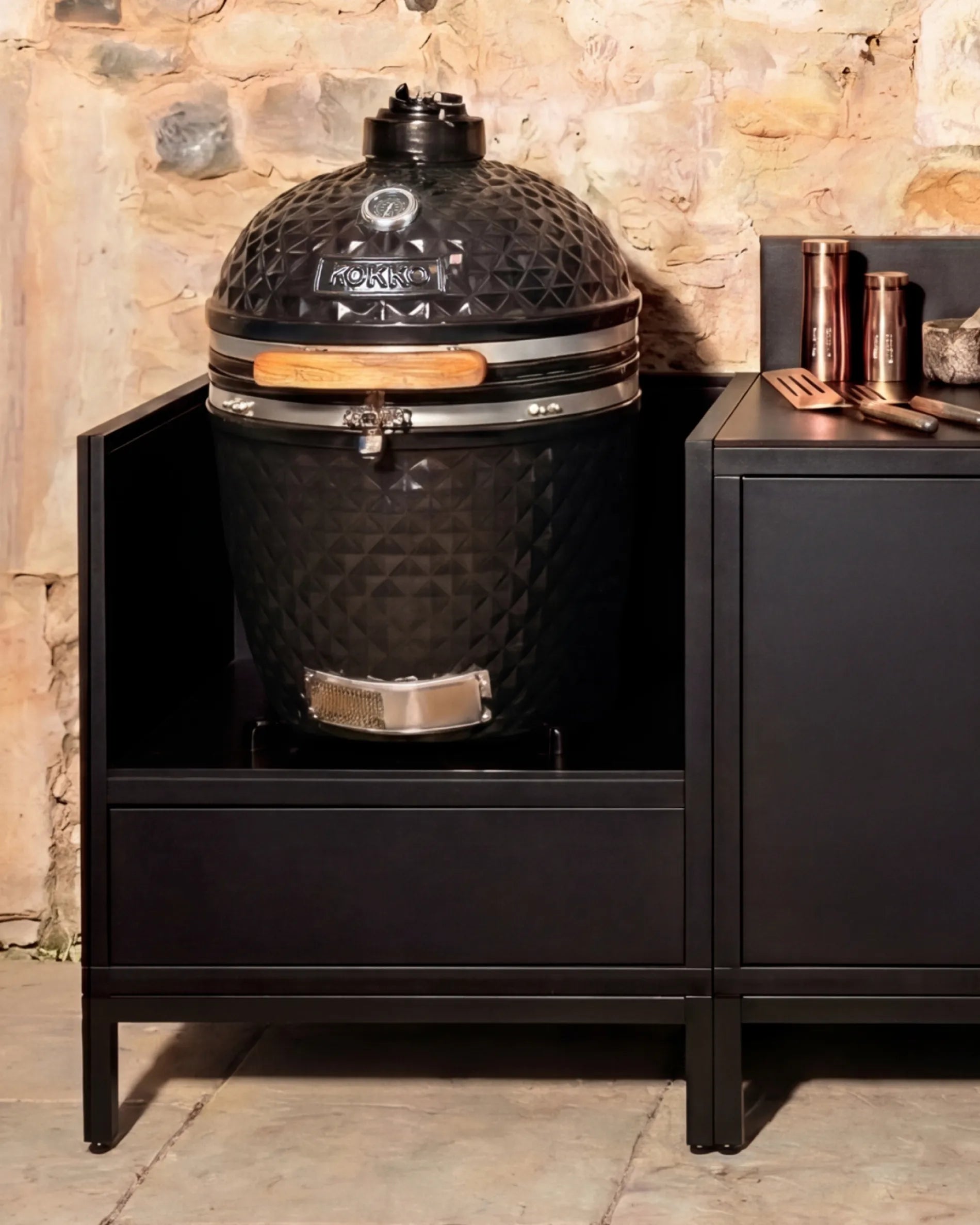 Schwarzer Kamado-Grill von Kokko, eingebaut im PILOTIS-Unterschrank mit Kupferzubehör – für stilvolles Outdoor-Kochen