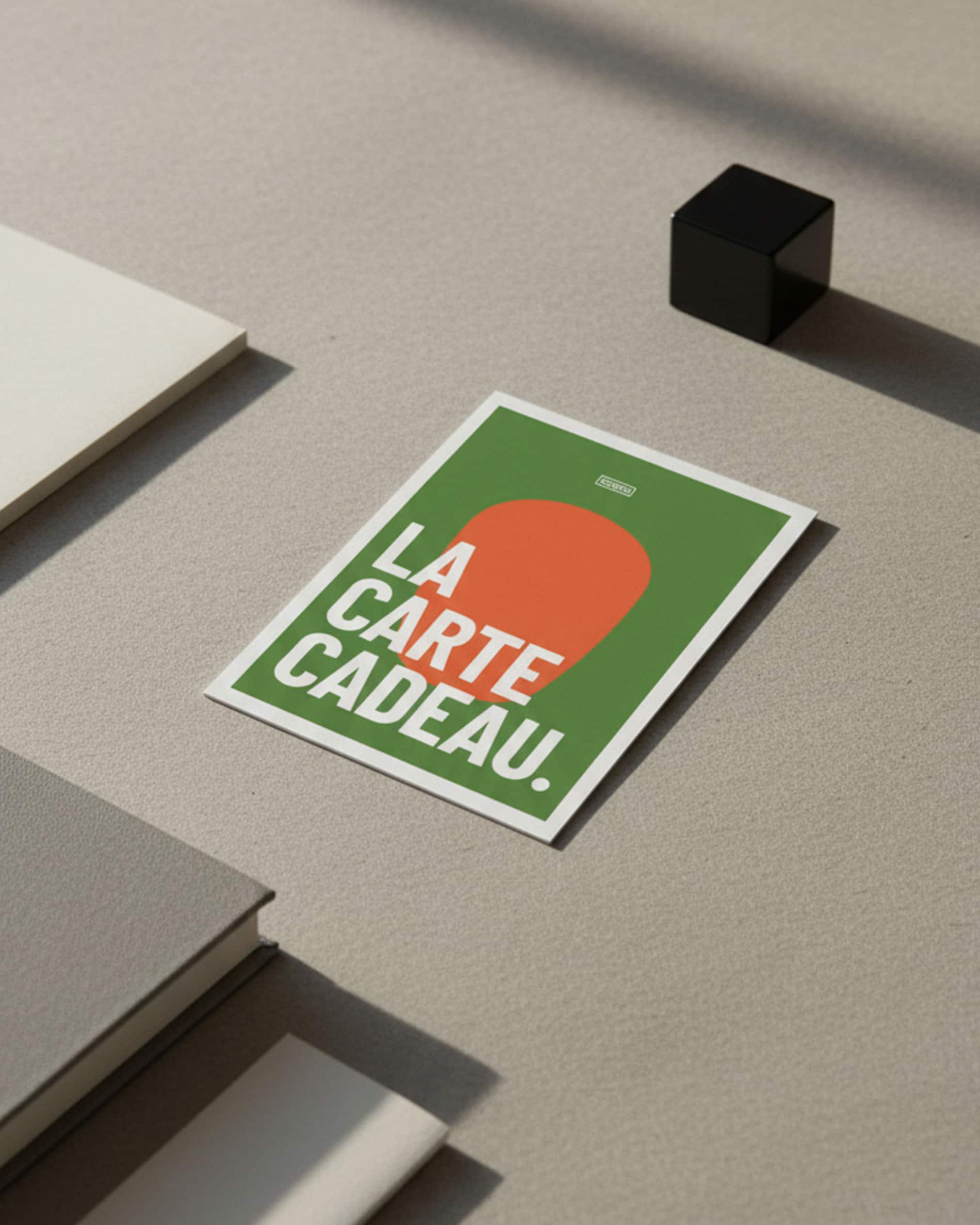 Kokko Geschenkkarte auf einer mineralischen Oberfläche, grafisches Motiv in Grün und Orange mit dem Text „die Geschenkkarte“.