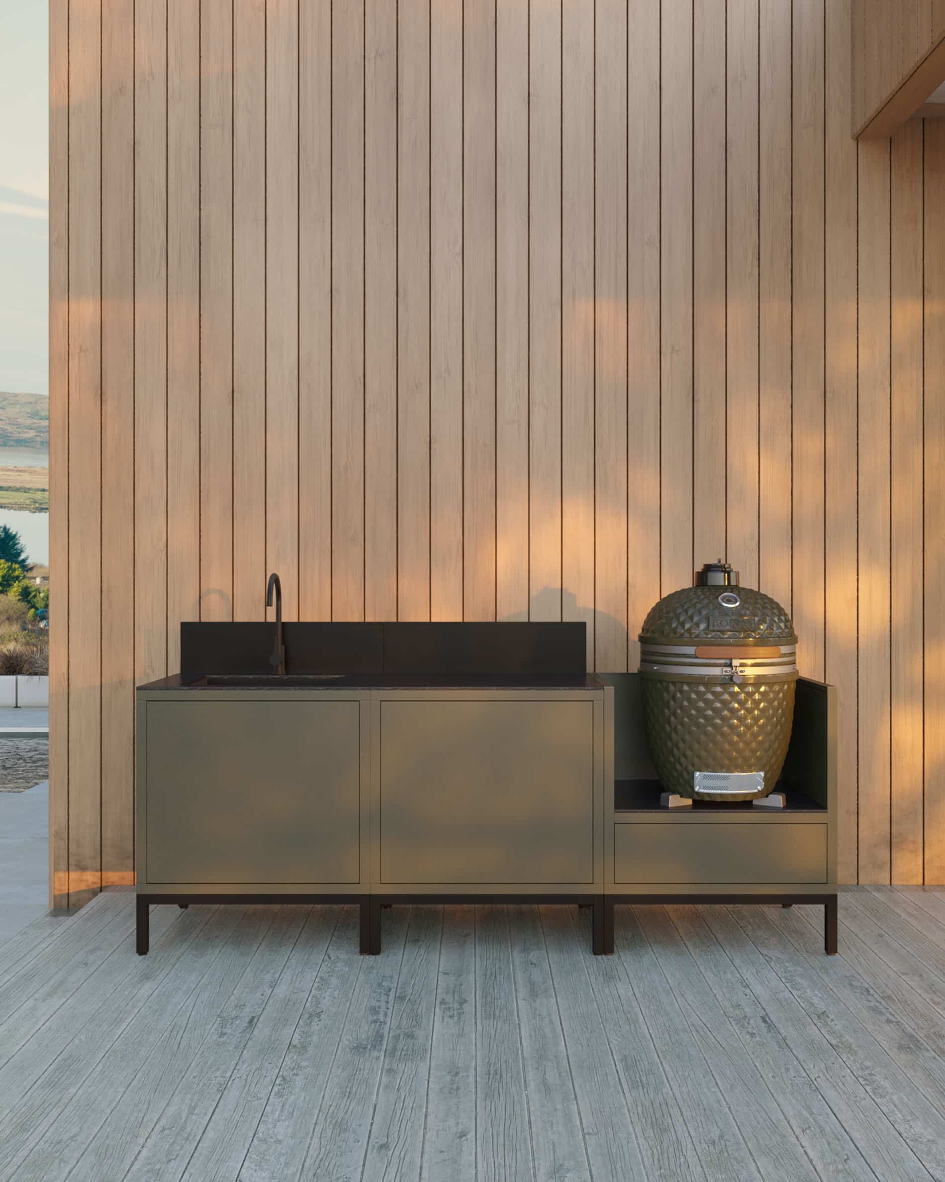 Outdoor-Küchenzeile auf Stelzen mit 3 Modulen für Kamado, integriertem Spülbecken, Möbel in Olivfarbe mit passender Arbeitsplatte und Rückwand, Spülbecken mit Wasserhahn links, zwei geschlossene Stauraummodule in der Mitte und integrierter Kamado im rechten Seitenmodul, Gestell mit schwarzen Füßen, Installation im Freien an einer Holzverkleidungswand.
