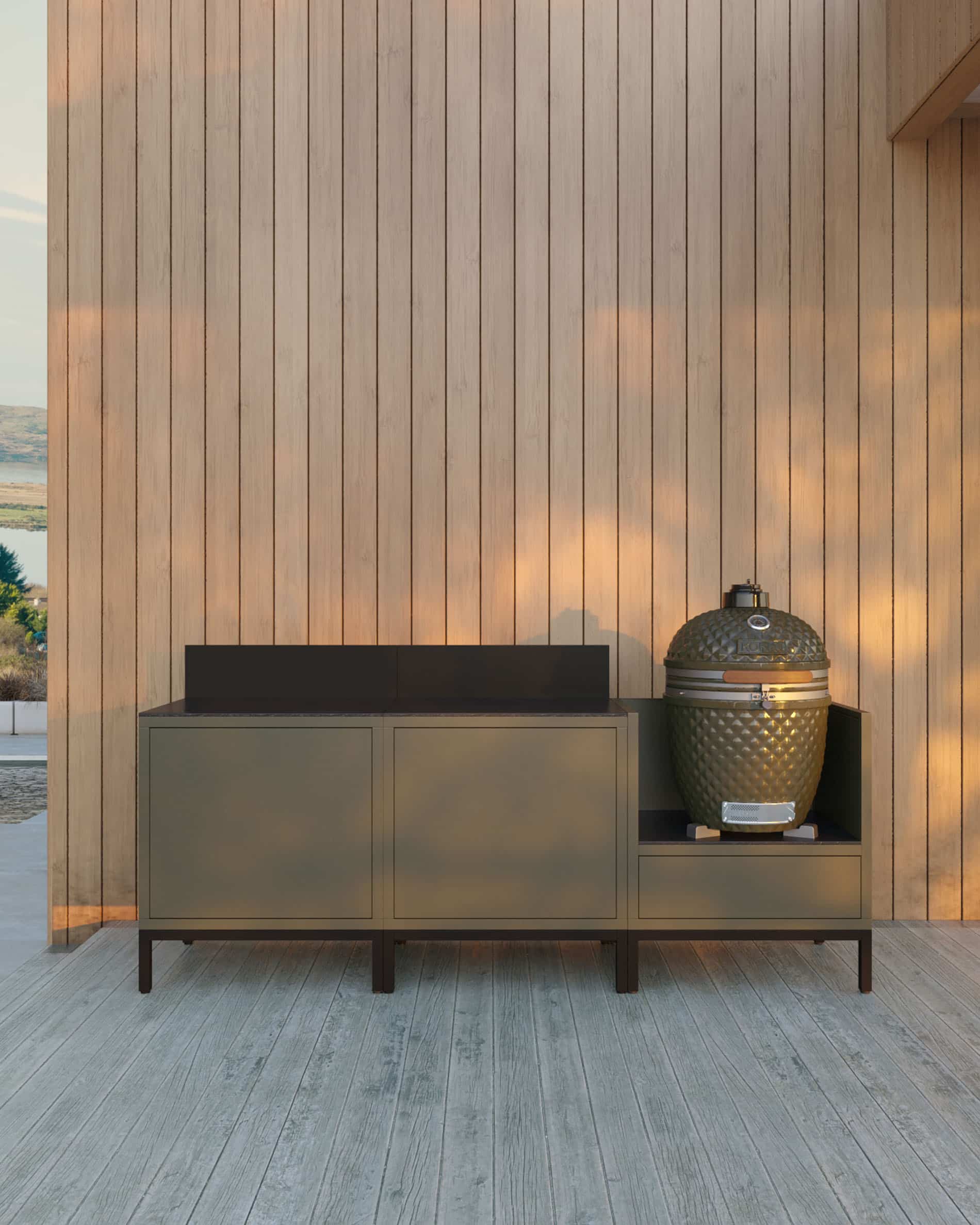 Outdoor-Küche auf Stelzen mit 3 Modulen für Kamado, Möbel in Olivgrün mit dunkler Arbeitsplatte und passender Rückwand, zwei geschlossene Aufbewahrungsmodule links und integrierter Kamado im rechten Seitenmodul, Konstruktion auf schwarzen Füßen, Installation im Freien an einer Holzfassade.