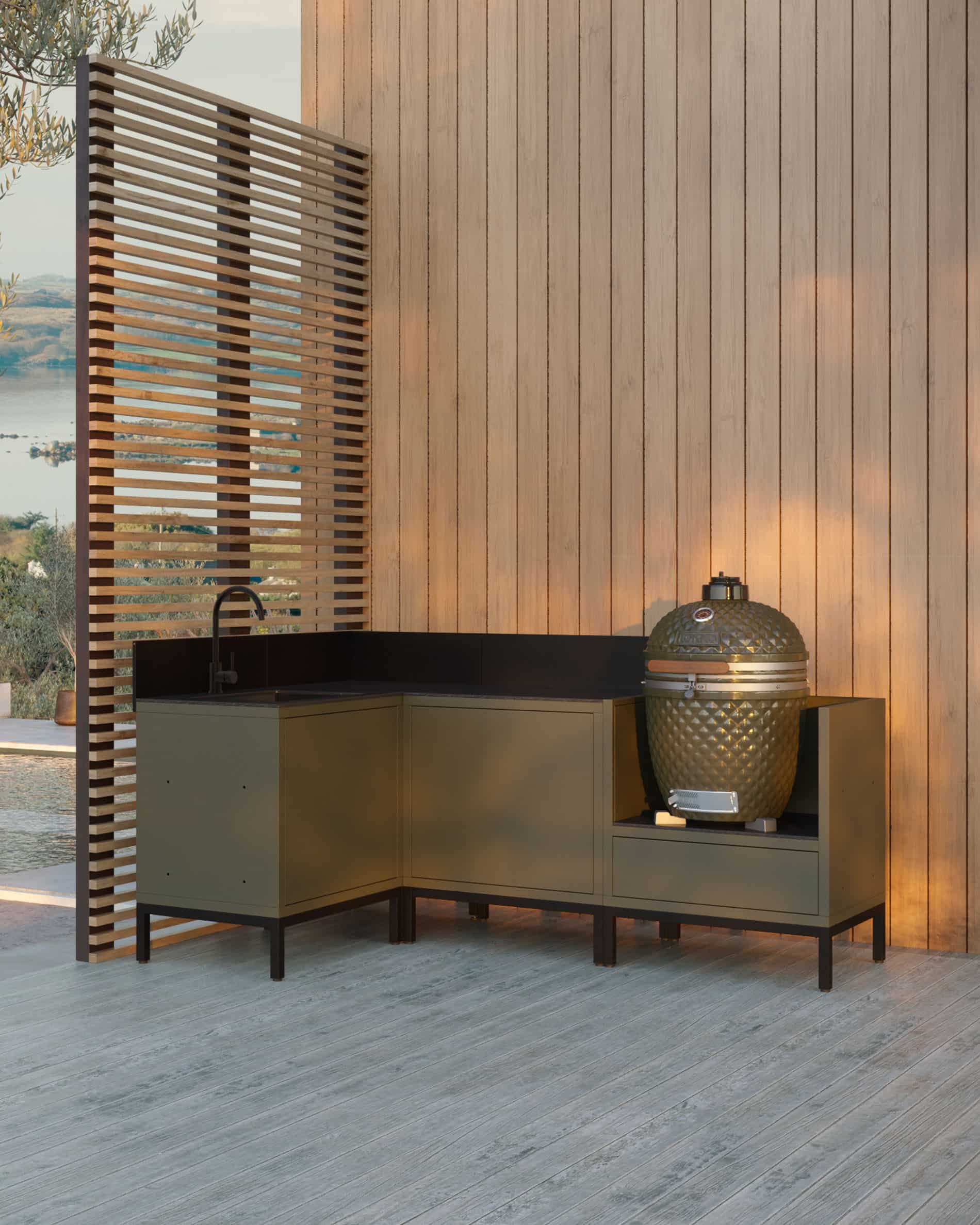 Eck-Außenküche auf Stelzen in Olivgrün, bestehend aus vier Modulen mit integriertem Spülbecken, schwarzer Arbeitsplatte und Platz für den Kamado, auf einer Holzterrasse vor einer vertikalen Holzverkleidung installiert.