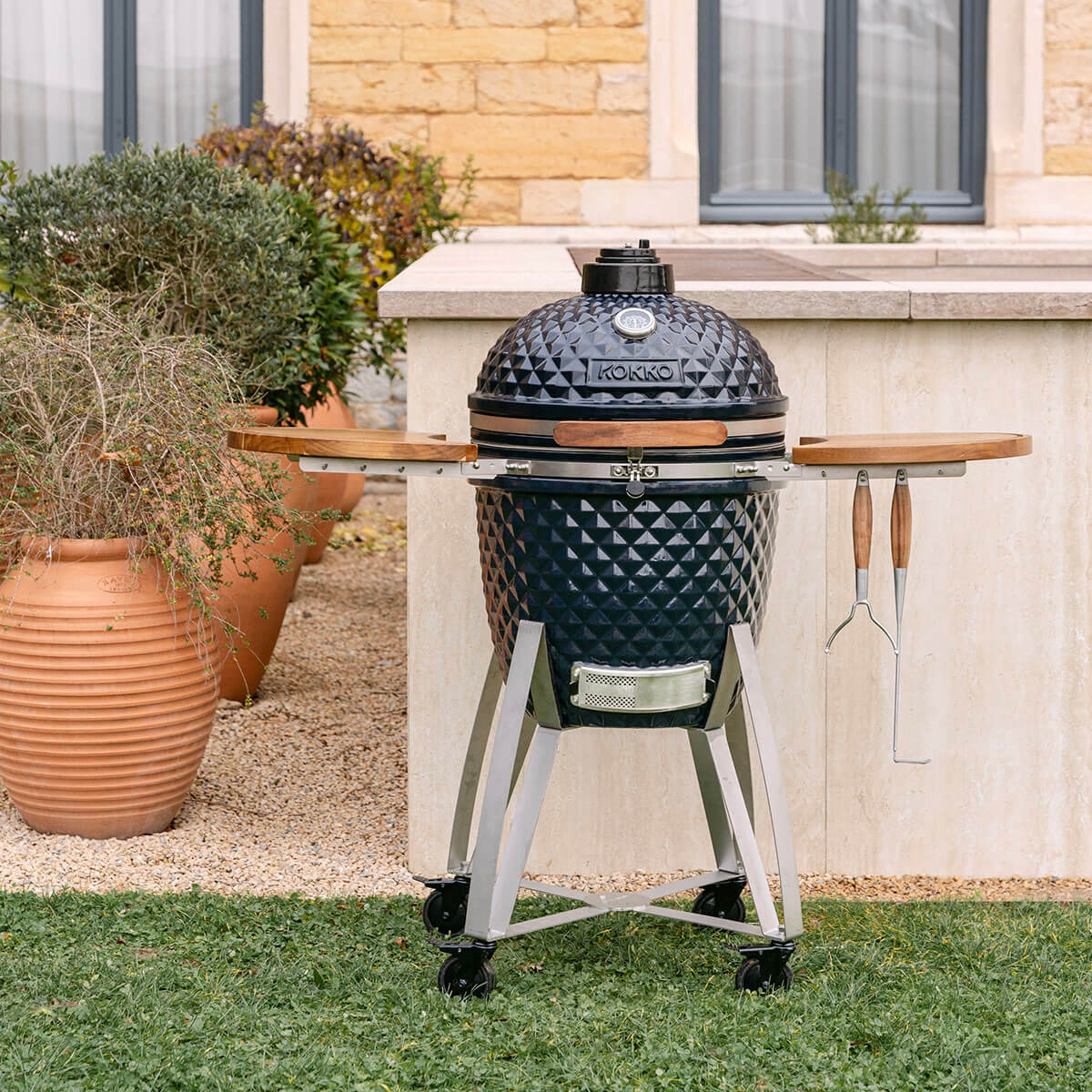 Kamado Kokko in Navy aus Keramik, ausgestattet mit Holzablagen und mobilem Gestell mit Rollen.