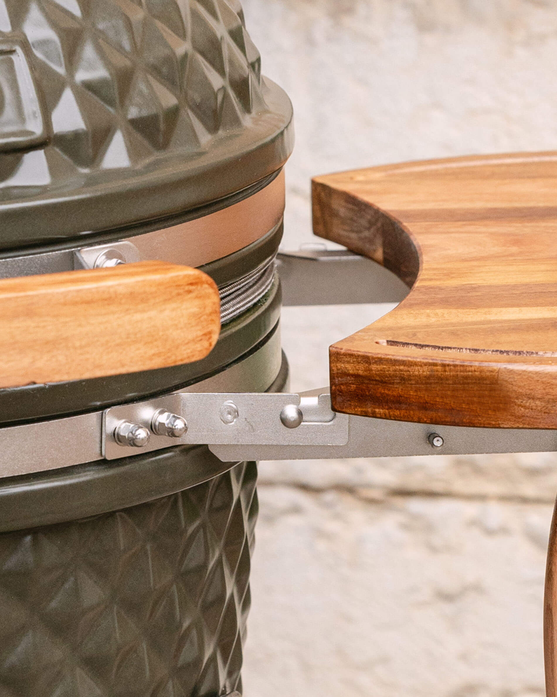 Nahaufnahme der Metallbefestigung, die das seitliche Holztablett mit dem Kamado verbindet, mit Fokus auf das Befestigungssystem und die Schrauben.