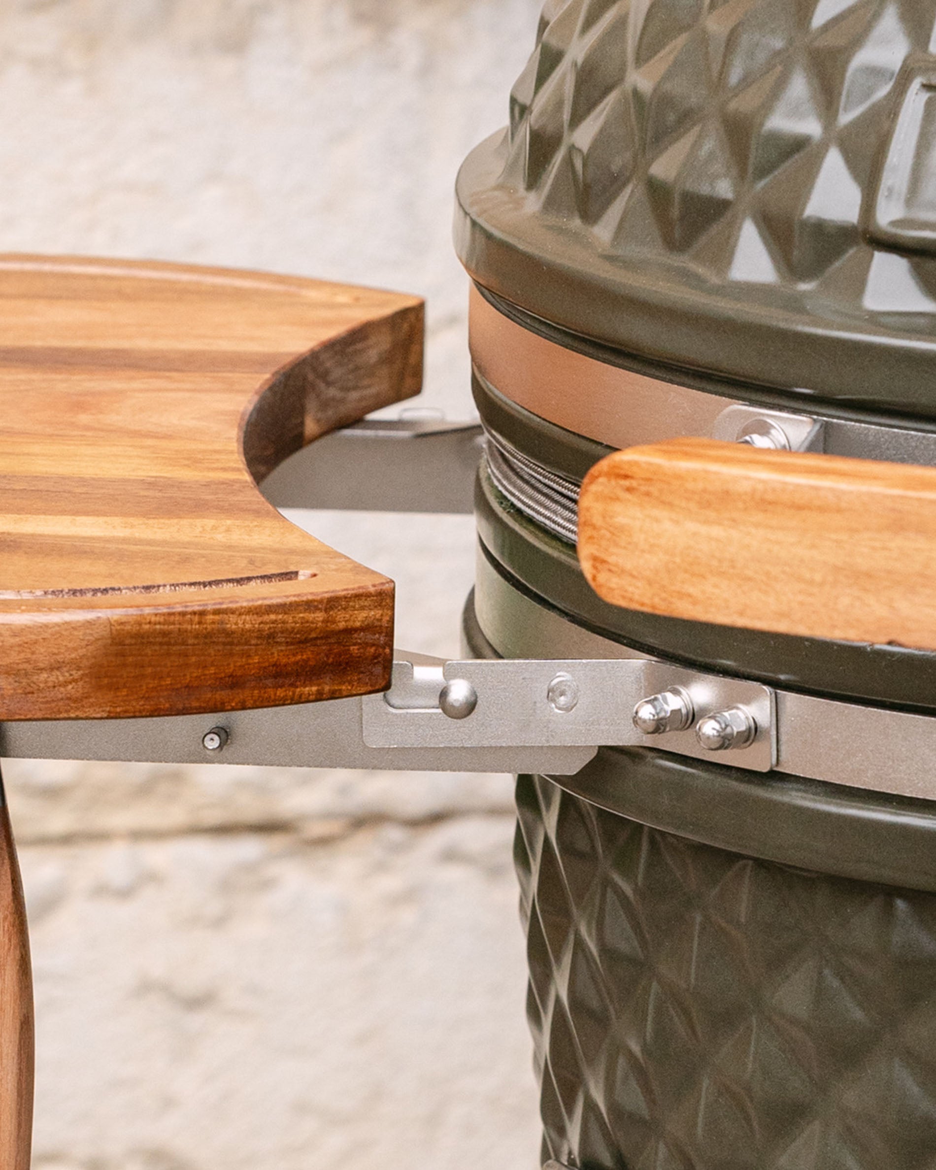 Detail der Metallbefestigungen, die das seitliche Holztablett mit dem Kamado verbinden, mit sichtbarem Holzgriff und Edelstahlring.