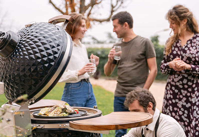 Eine Gruppe von Freunden versammelt sich um einen Kokko Kamado bei einem Essen im Freien – ein Moment voller Genuss und Geselligkeit.