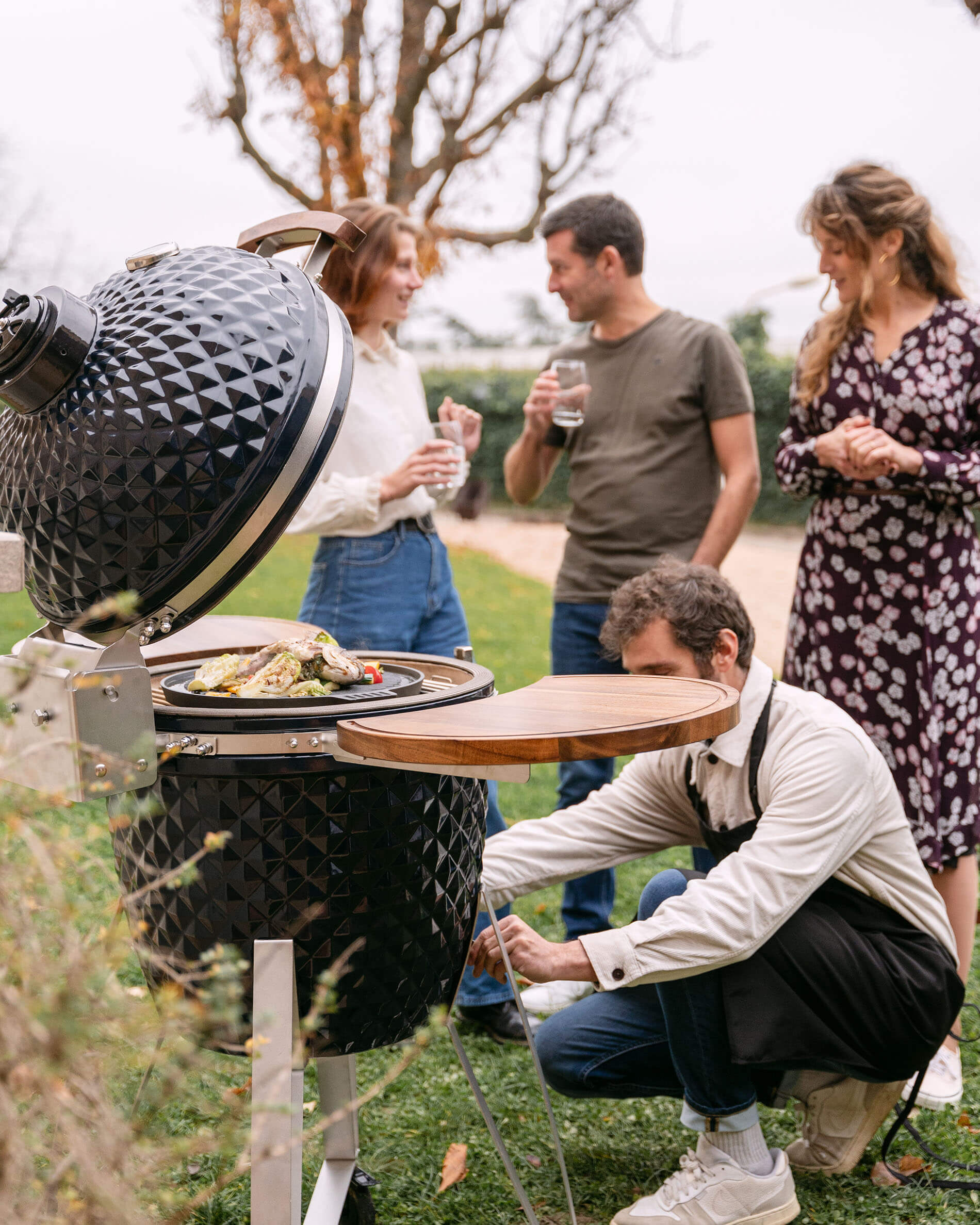 Kamado-Grill Kokko 22 Zoll aus Keramik in Marineblau bei einem geselligen Moment im Freien verwendet.