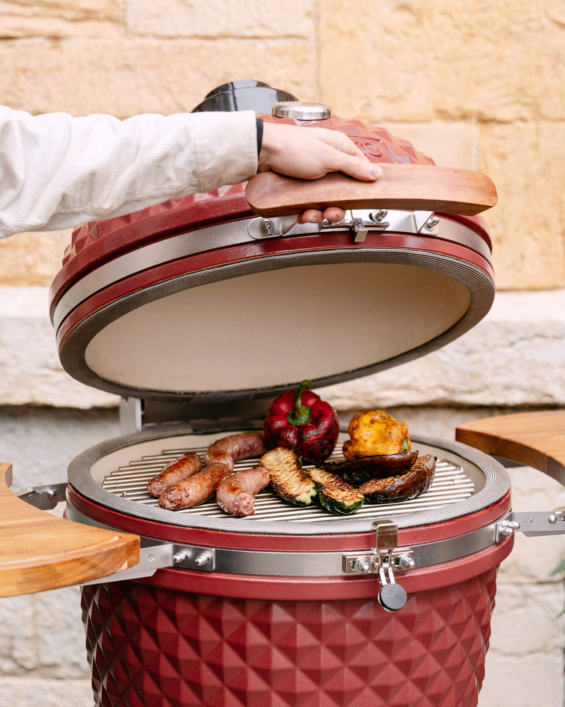 Geöffneter roter Kamado Kokko 22 Zoll aus Keramik, mit Würstchen und Gemüse auf dem Grillrost.