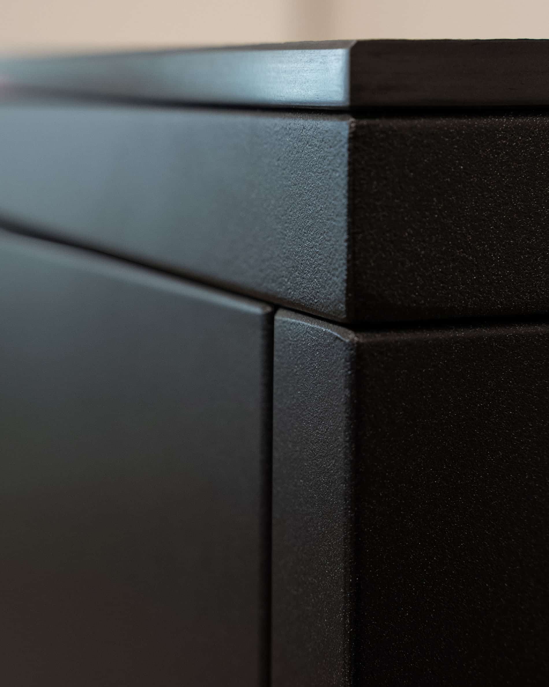 Detail einer Pilotis-Außenküche, mit Fokus auf die Ecke des Möbels, die Verbindung der Paneele und die matte Struktur der dunklen Front.