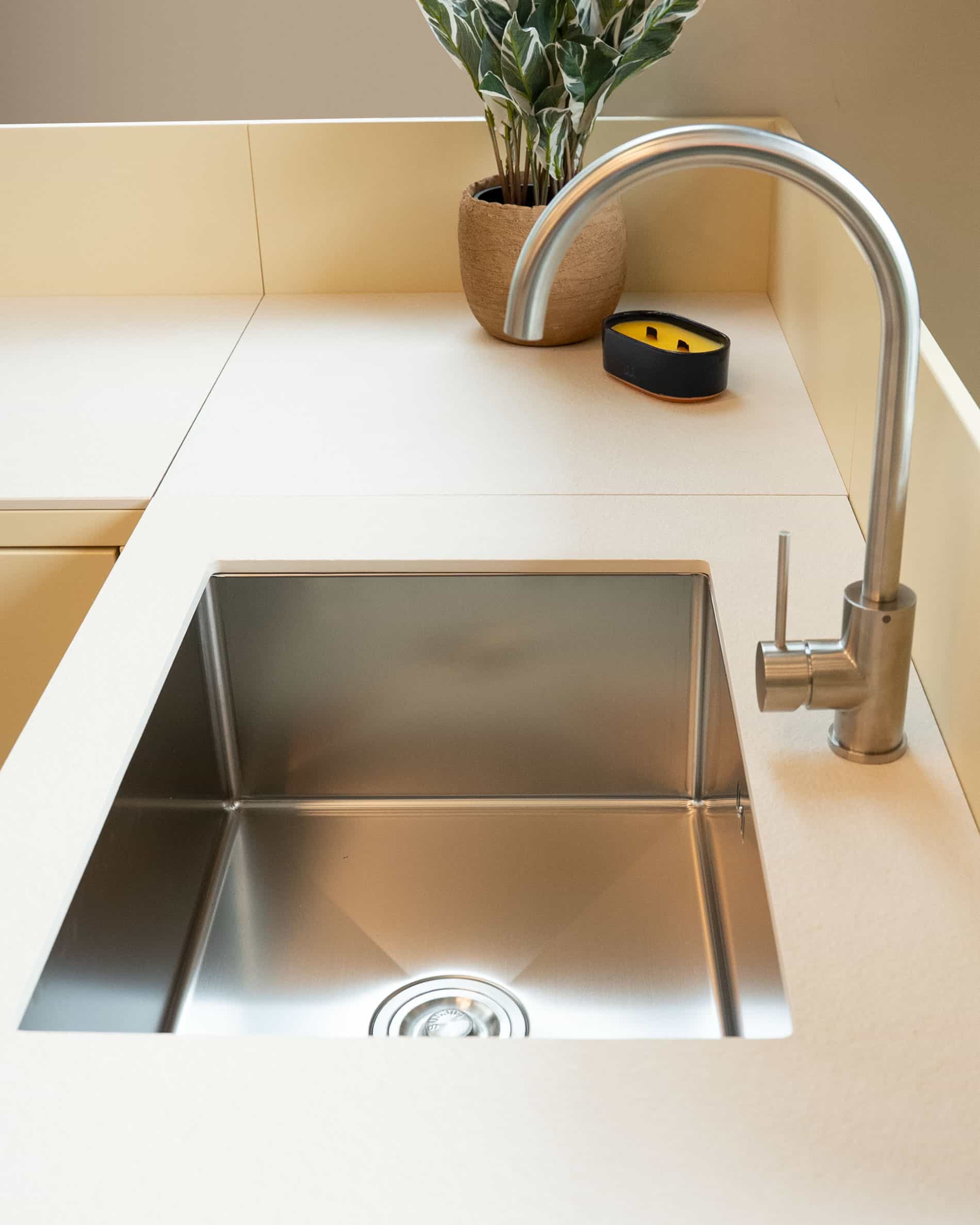 Detail des integrierten Spülbeckens einer Pilotis-Außenküche mit Edelstahlbecken, Armaturen aus Metall und cremefarbener Arbeitsplatte.