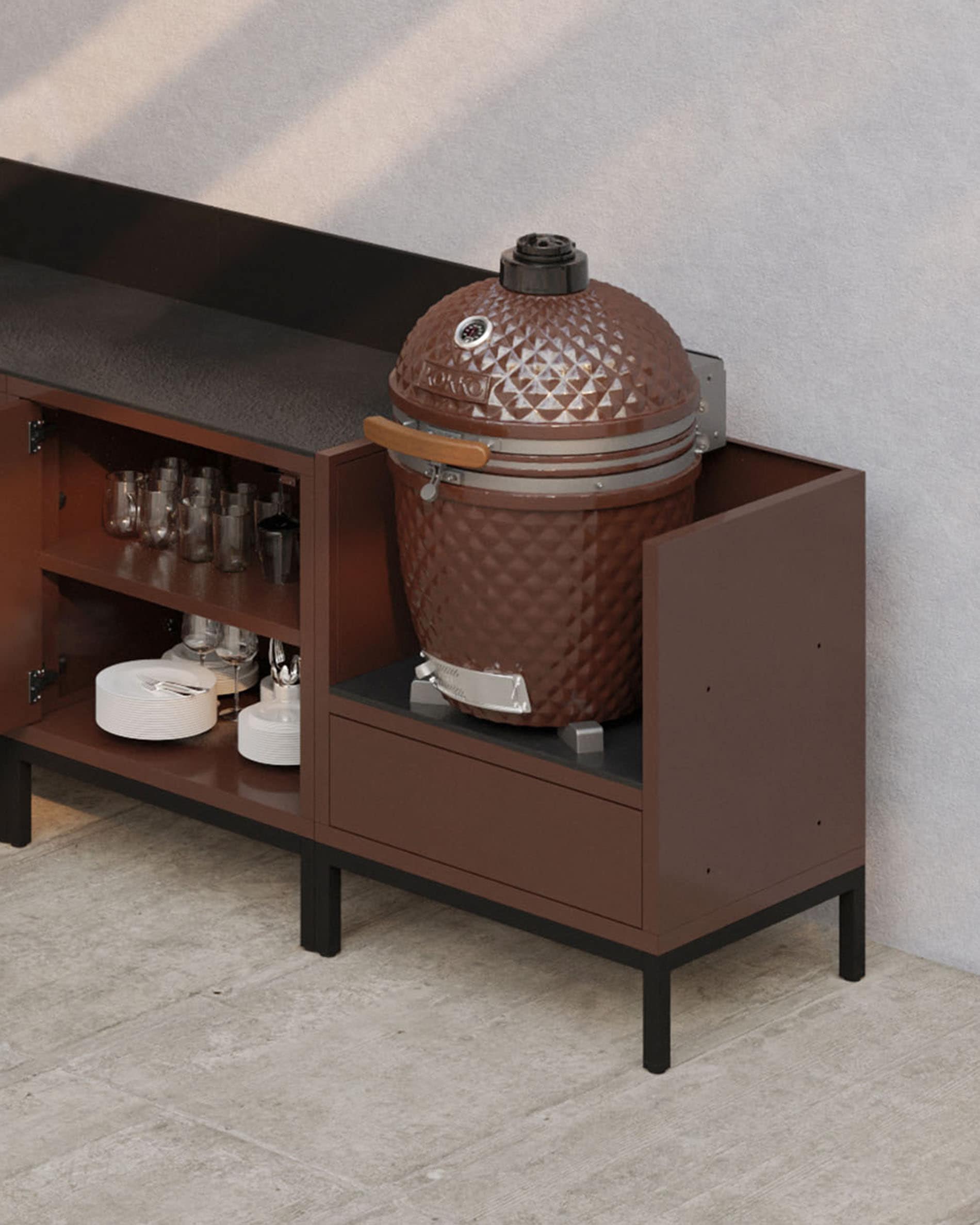 Modulare Outdoor-Küche auf Stelzen in Rostoptik mit dunkler Arbeitsplatte, offenen Ablagen und einem Modul für einen Kamado-Grill.
