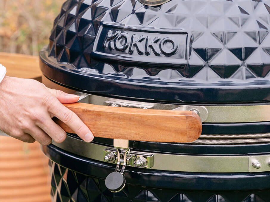 Poignée frontale en bois d’acacia du kamado Kokko nouvelle édition, fixée sur le couvercle en céramique noire.